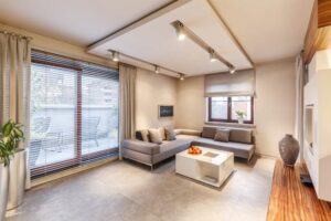 Spacious, brown living room interior design with sofa, table, lighting, large sliding balcony window and large shutter blinds
