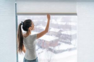 Woman closing her insulation blinds, with snow on the ground outside