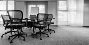 Black office chairs surrounding a small office table, with a whiteboard and white blinds decorating the windows