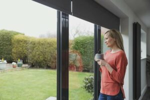 Woman looking outside her patio doors that are decorated with grey motorised blinds