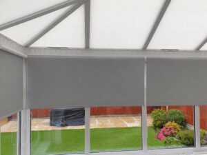 A set of gray roller blinds pulled down half way overlooking a garden in the background.