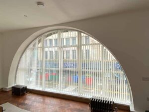 A set of white Vertical Blinds set up on an arched window