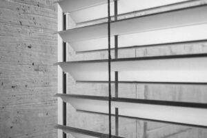 Closeup of a motorized Venetian blind in silver with a grey wall to the left.