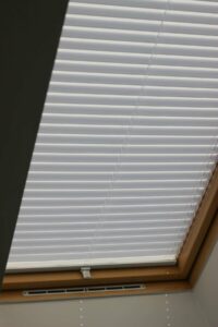 White and grey pleated blinds closed over a skylight window with a wooden frame.