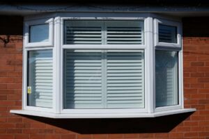 The outside of a house with shutters attached to bay windows.