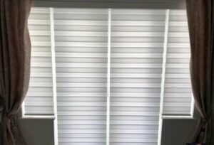 A set of closed day and night blinds inside a living room beside a pair of dark curtains.