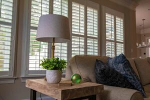 A pair of shutters placed on a high frame window with the blinds being open to allow light in the living room.
