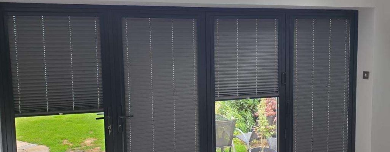 A set of perfect fit blinds attached to several doors and windows overlooking a garden area.