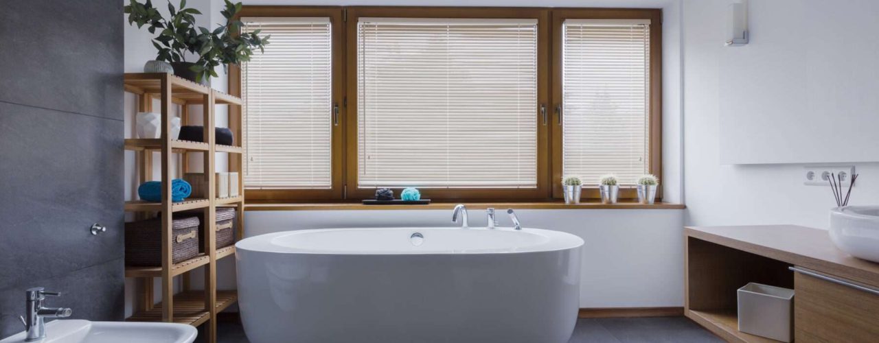 Spacious and comfortable bathroom with a freestanding bathtub in front of a set of closed blinds to block out the light from entering the room.