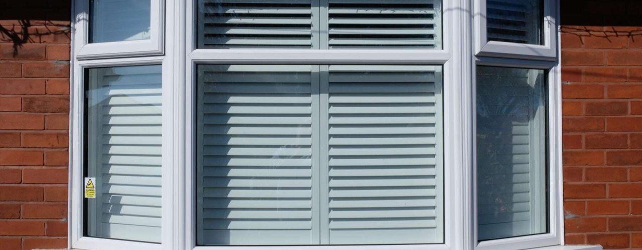 The outside of a house with shutters attached to bay windows.