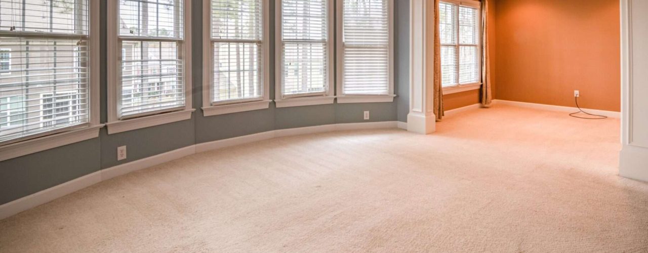 An open space living room with no furniture installed with the blinds open on the windows.