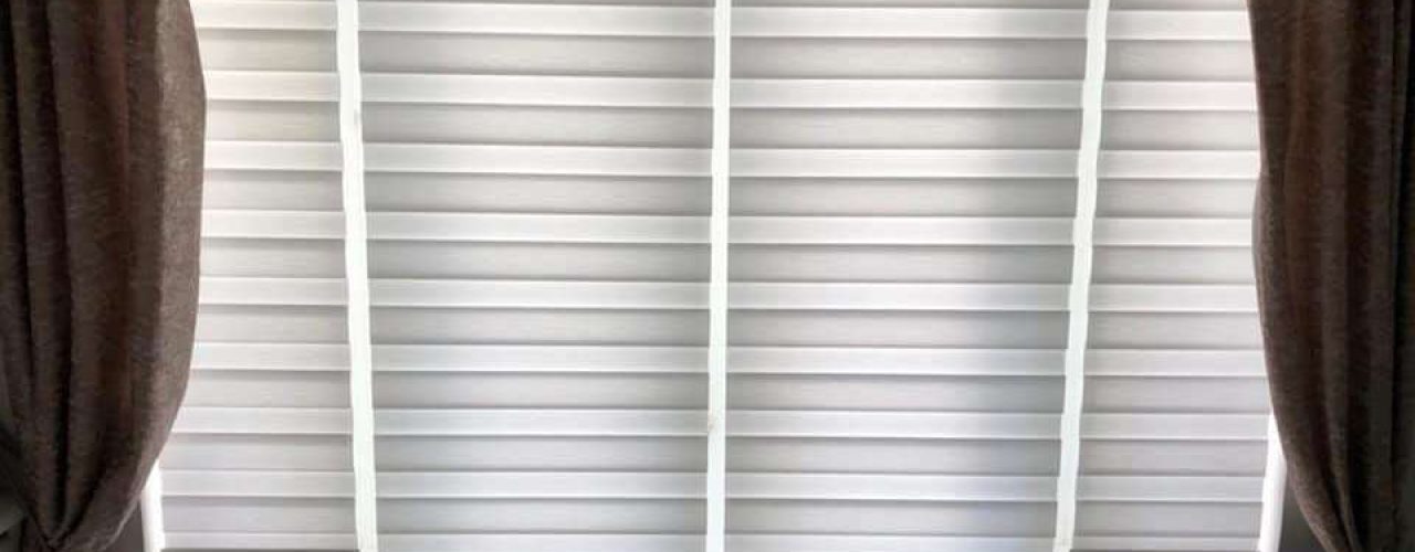 A set of closed day and night blinds inside a living room beside a pair of dark curtains.