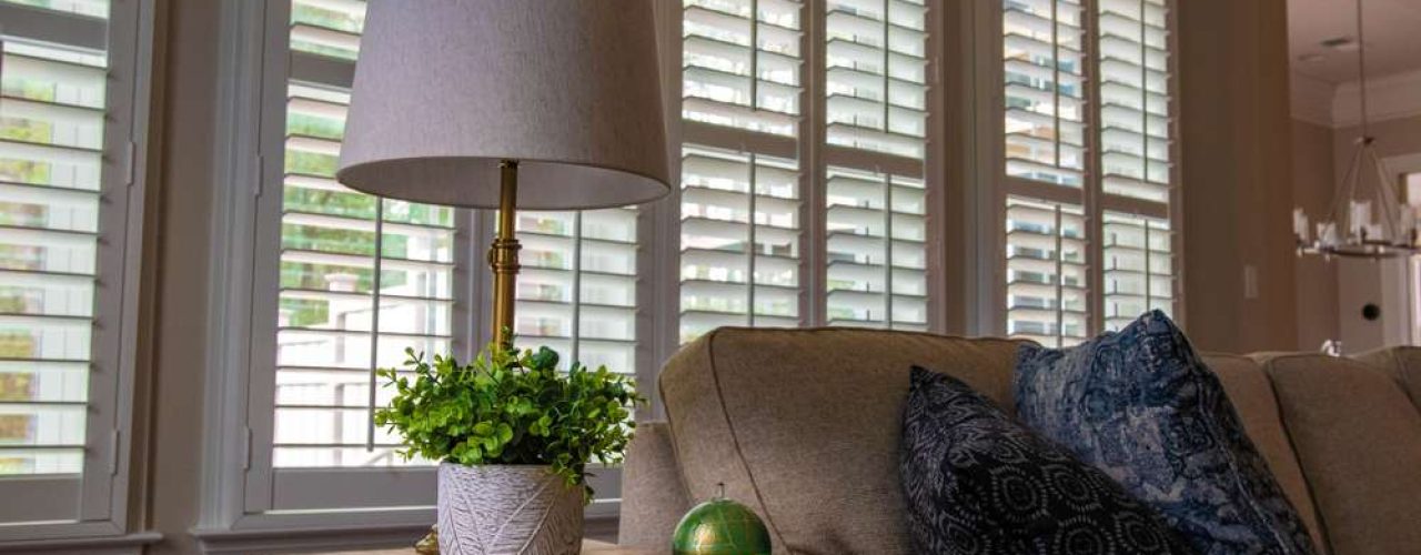 A pair of shutters placed on a high frame window with the blinds being open to allow light in the living room.