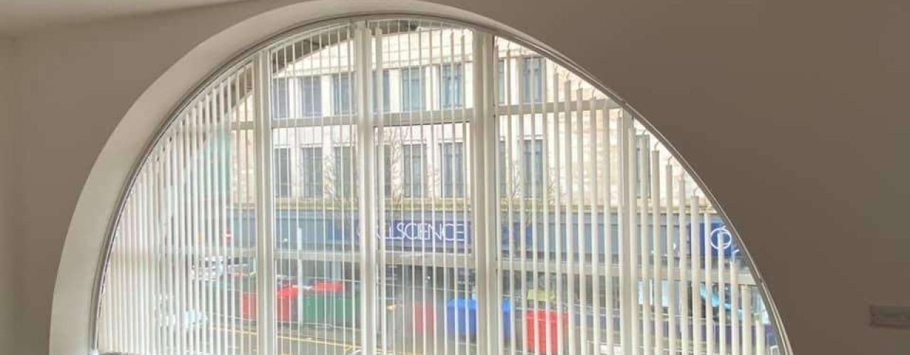 A set of white Vertical Blinds set up on an arched window