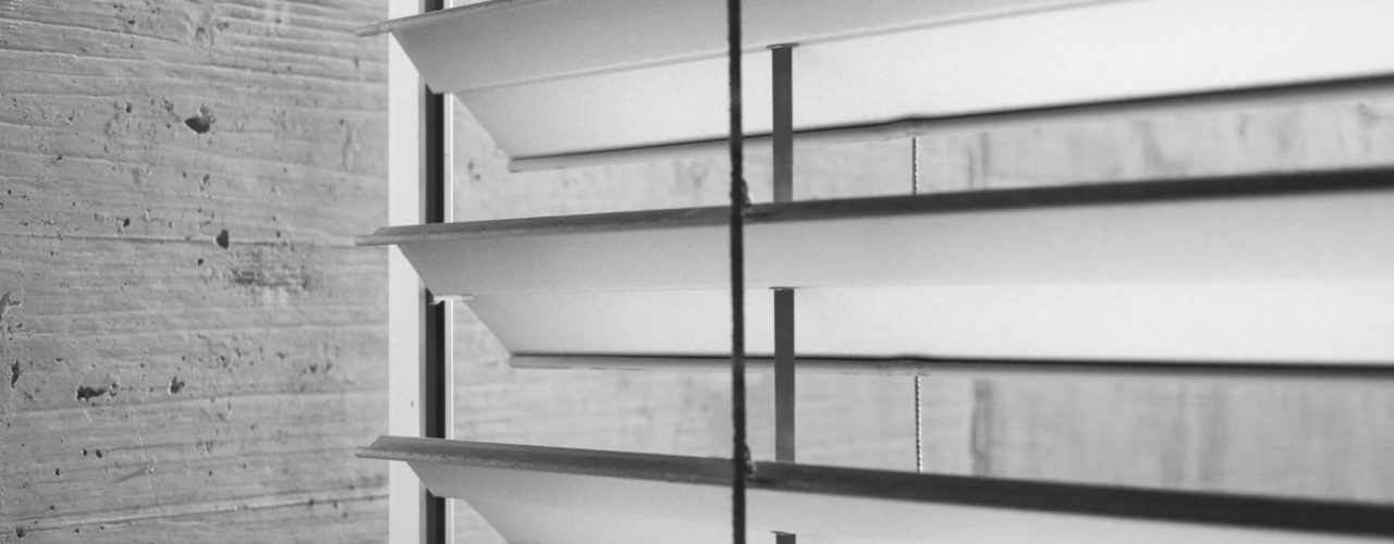 Closeup of a motorized Venetian blind in silver with a grey wall to the left.