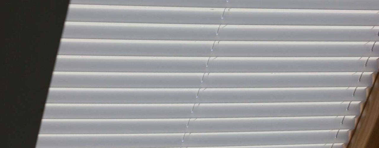 White and grey pleated blinds closed over a skylight window with a wooden frame.