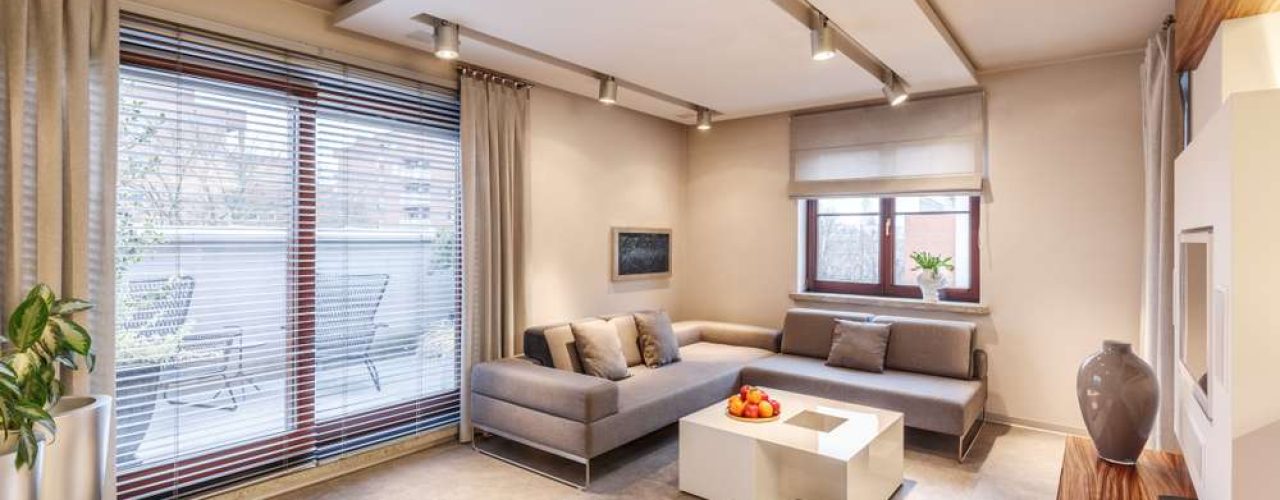 Spacious, brown living room interior design with sofa, table, lighting, large sliding balcony window and large shutter blinds
