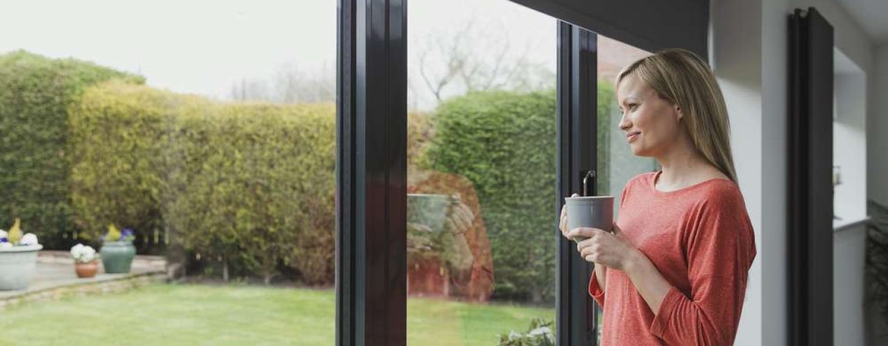 Woman looking outside her patio doors that are decorated with grey motorised blinds